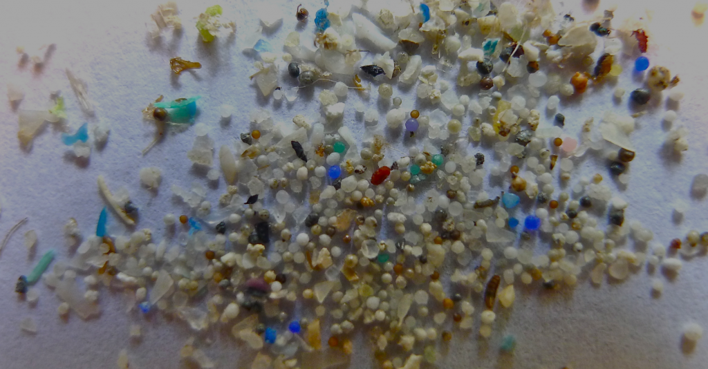 Vários microplásticos (pedaços pequenos de plástico) espalhados sob uma superfície branca.