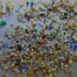 Vários microplásticos (pedaços pequenos de plástico) espalhados sob uma superfície branca.