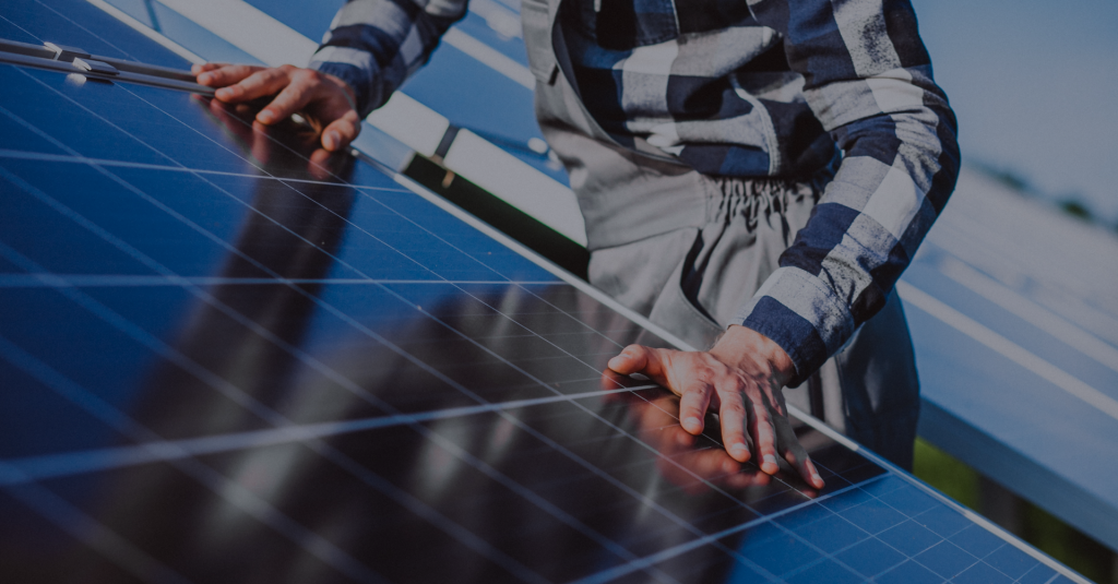 Imagem mostra mãos de um homem em cima de um painel de energia solar.