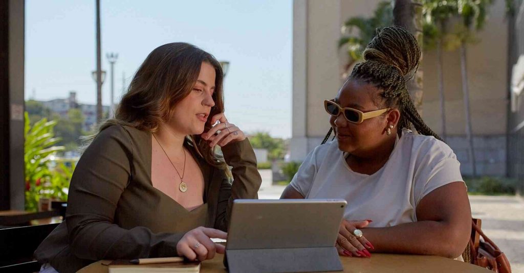 Duas mulheres conversam enquanto olham para a tela de um tablet sobre a mesa