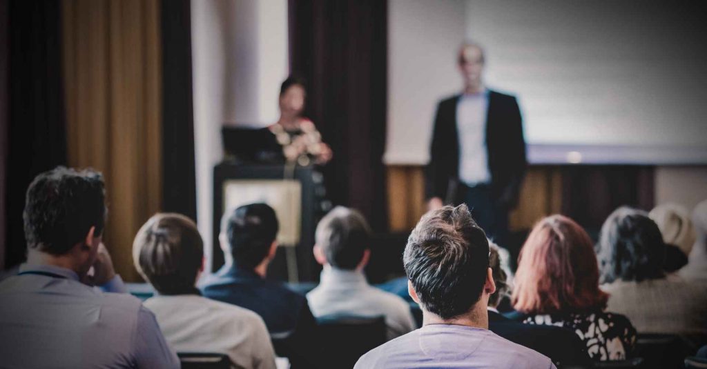 Profissionais de costas acompanhando palestra